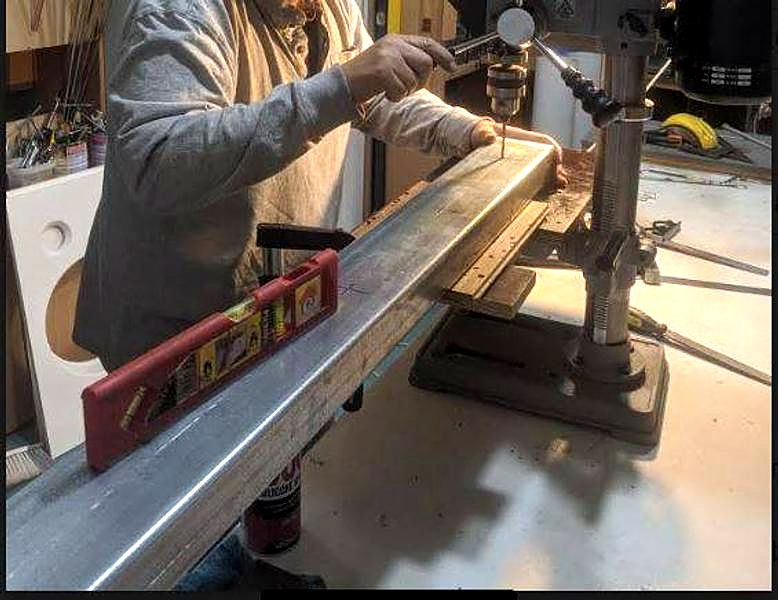 A long metal channel on a bench drill press, with a red spirit level resting on it.