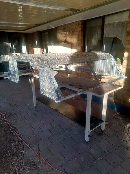 An aluminium checker-plate frame resting on metal stands under a patio.